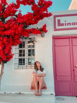 A woman gazes up while sitting on mediterranean steps under vivid red blossoms.