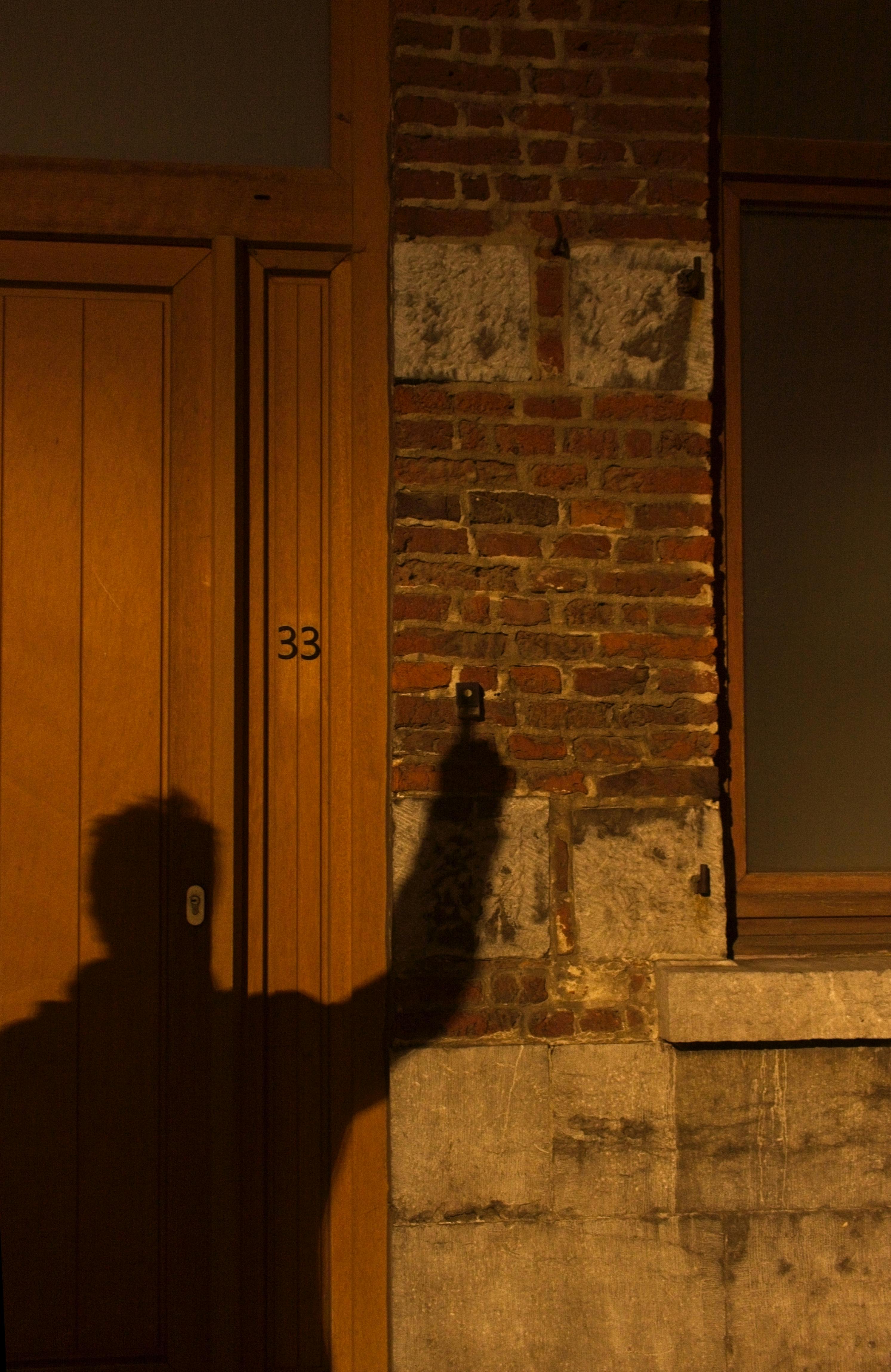 Silhouette of individual against a red brick wall near a wooden door at night.