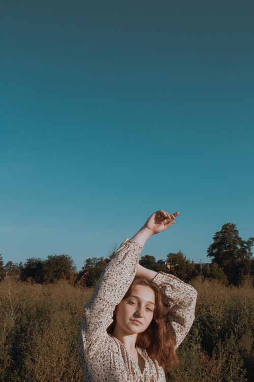 Free Woman in a sunlit meadow with arms raised, enjoying nature. Stock Photo