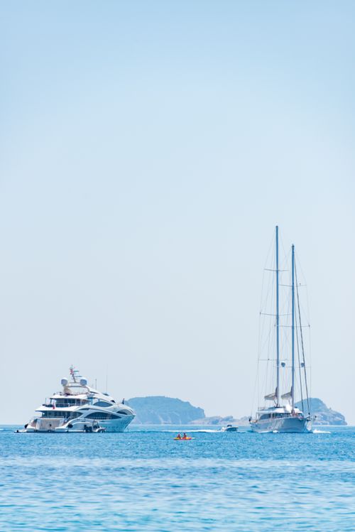Free Elegant yachts sailing in calm blue waters near a distant island under a clear sky. Stock Photo