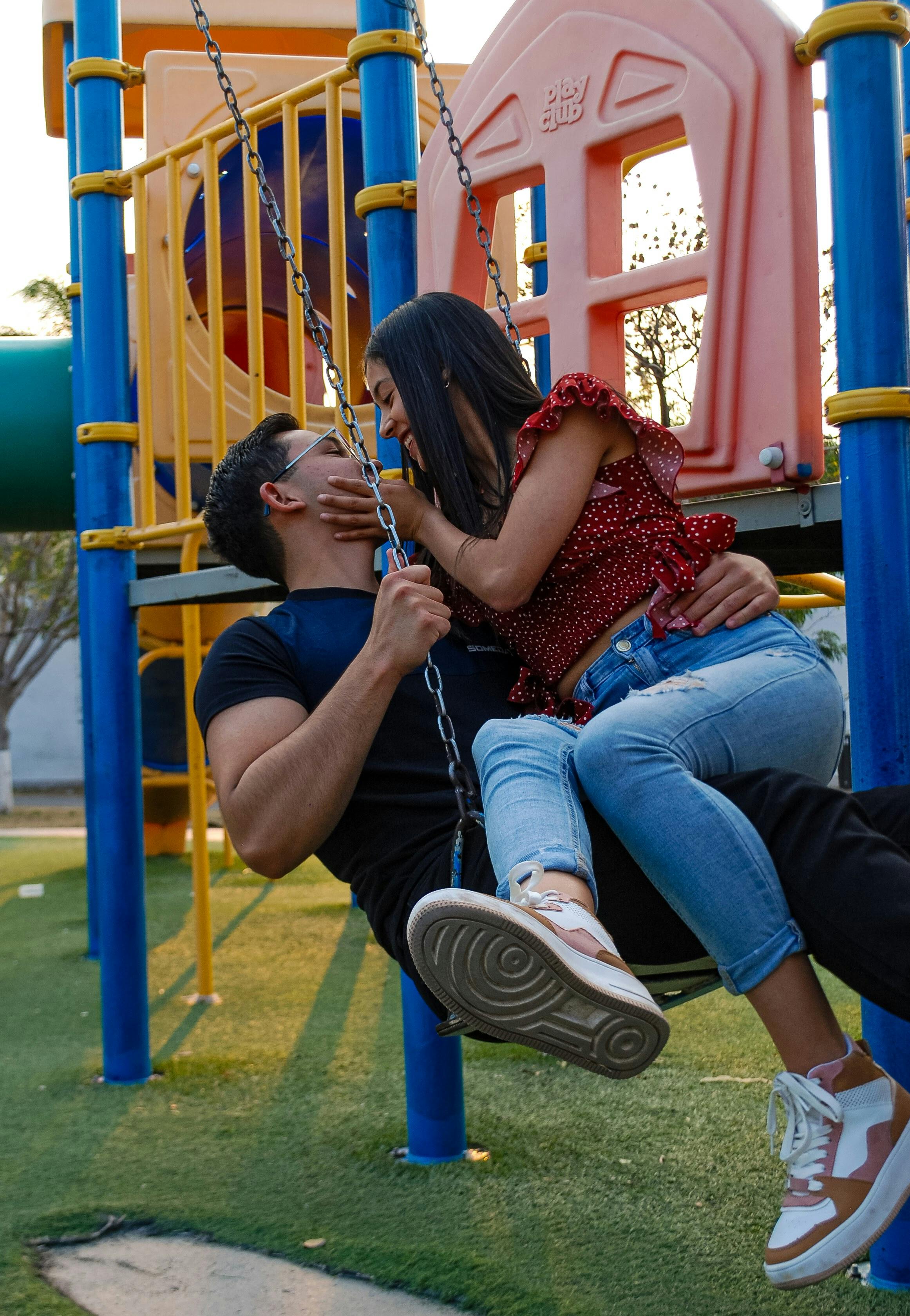 A happy couple kissing on a swing at the playground during sunset, embracing love and joy.