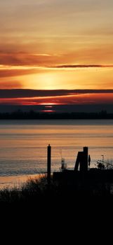Beautiful sunset over a peaceful lake with silhouettes of a pier and trees. Captures nature's tranquility.