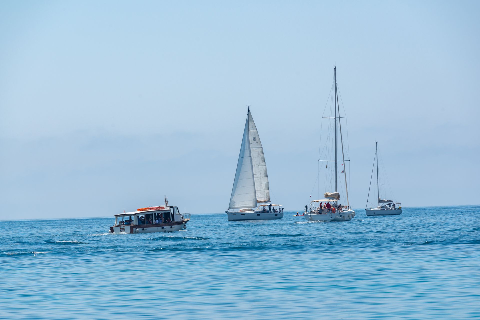 Sailboats and a motorboat on open water under a clear blue sky