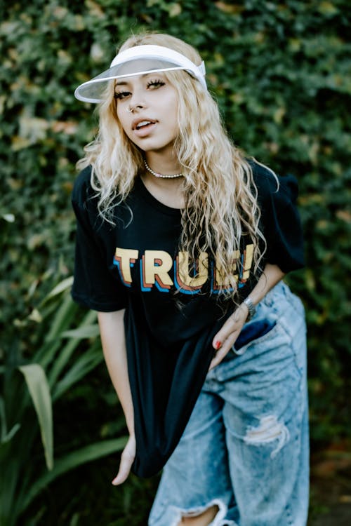 Young Woman in a T-shirt, Jeans and a Visor Standing Outside 