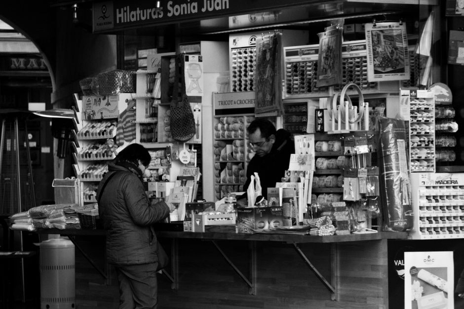 Vista en blanco y negro de un puesto de mercado en Valencia con clientes interactuando.