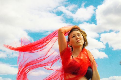 Free Portrait of a woman posing with a red veil against a cloudy sky, exuding elegance. Stock Photo