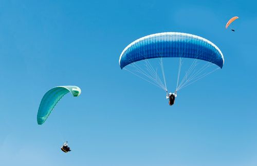 Free Three paragliders soaring gracefully under a clear blue sky, capturing the essence of adventure. Stock Photo