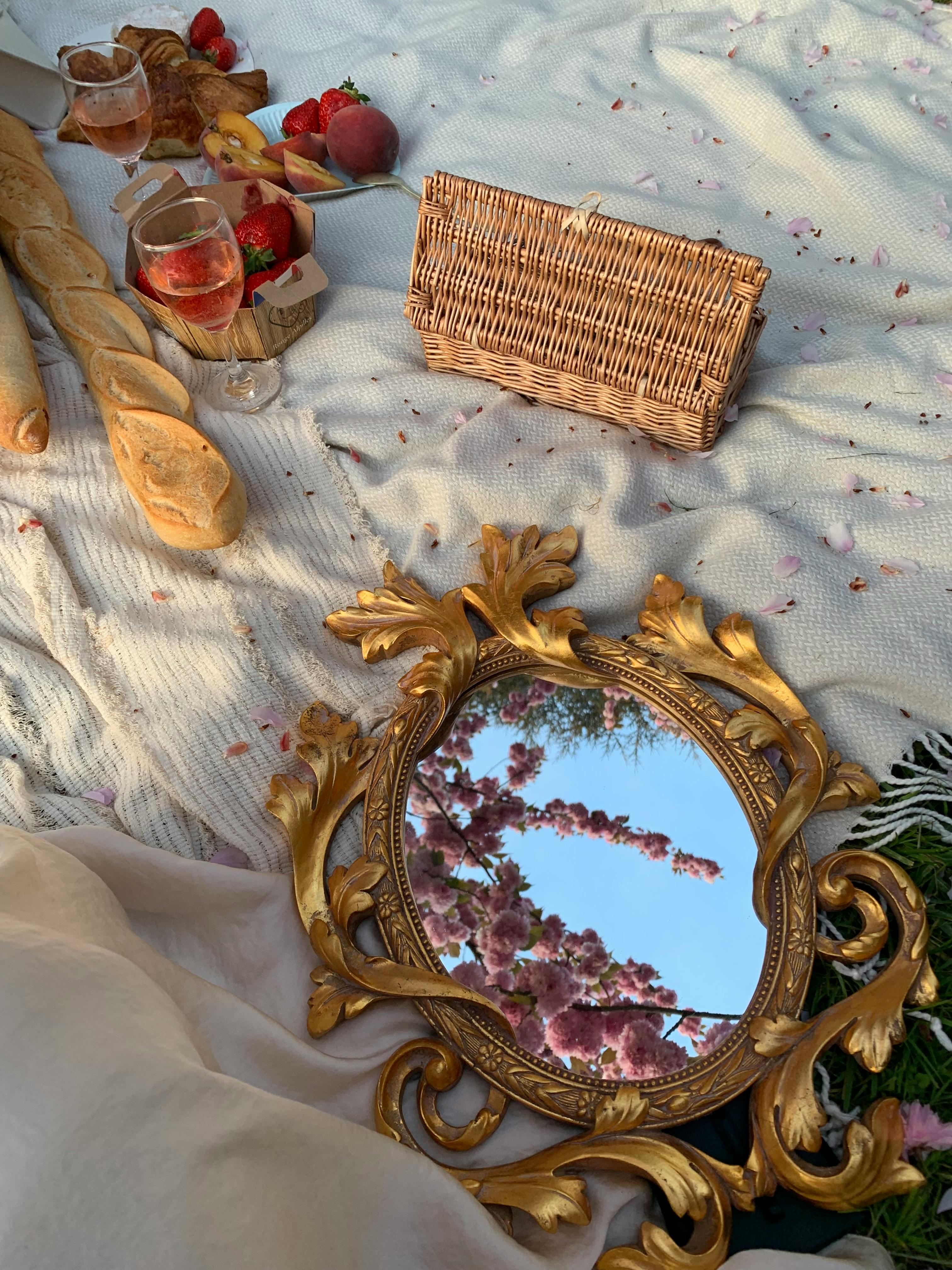 A charming picnic setup featuring baguettes, strawberries, wine, and a decorative mirror reflecting cherry blossoms.