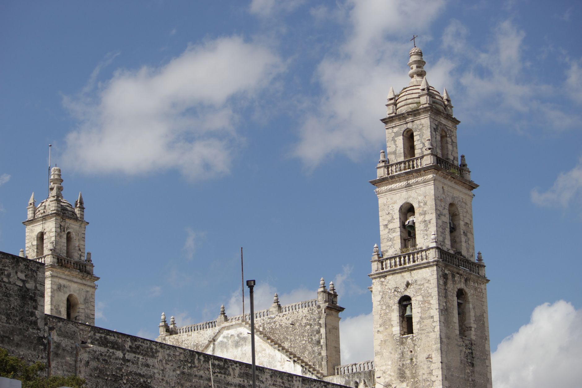 The pale stone twin bell-towers of Mérida's San Ildefonso Cathedral rising against a blue Yucatán sky, with the crenellated roofline of the nave between them