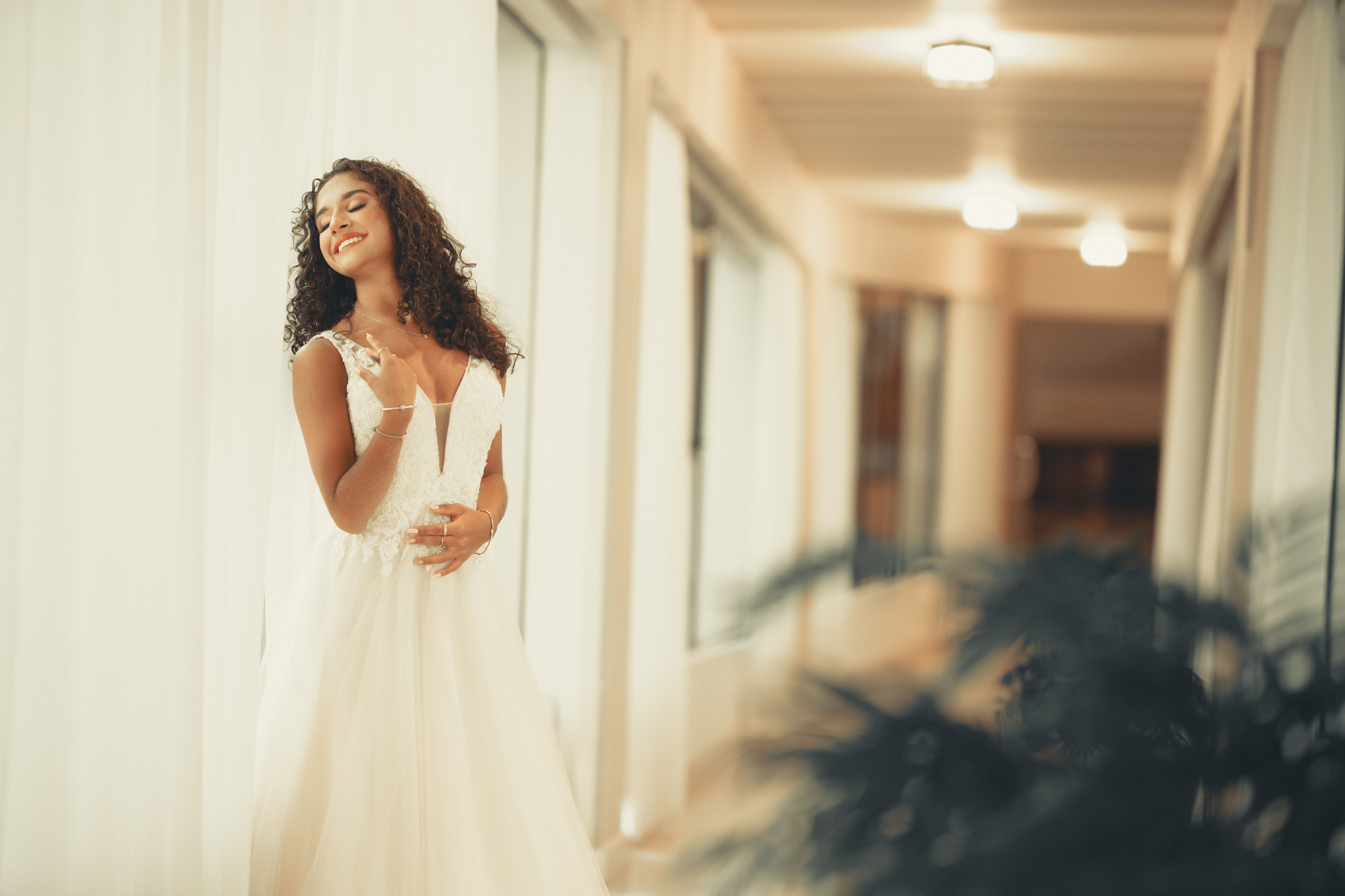 Portrait of a smiling woman in a white dress posing in an elegant indoor corridor.