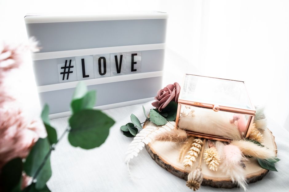 Charming still life setup with love sign, decorative box, and floral accents on a wooden base.