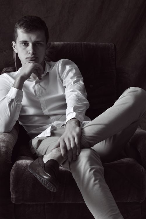 Free An elegant and thoughtful young man sits confidently in a velvet armchair, in a black and white portrait. Stock Photo
