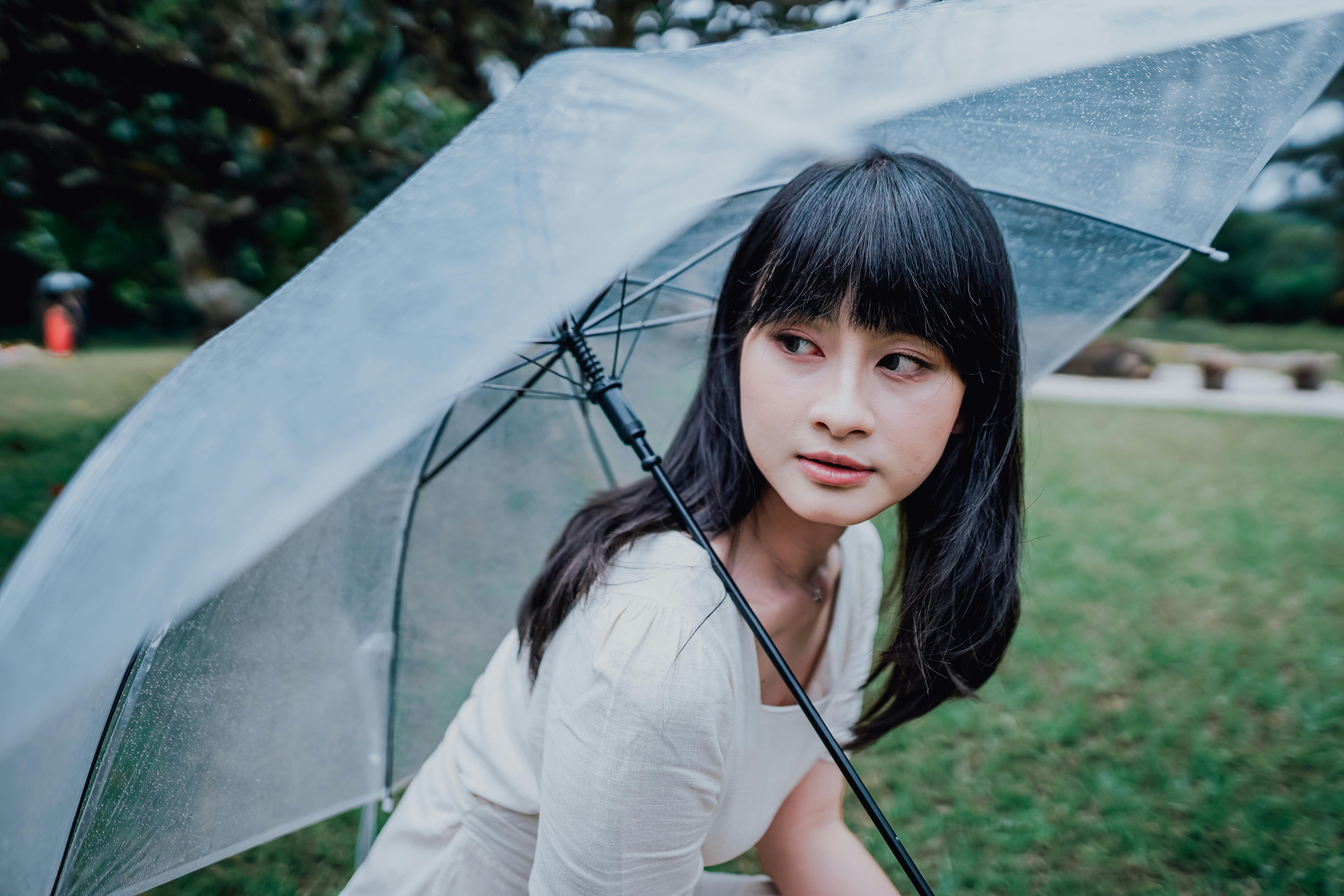 Asian woman with clear umbrella in a lush park, enjoying the rainy day.