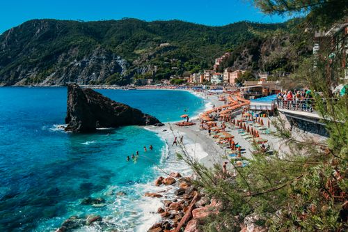 Free Picturesque beach with umbrellas, crystal clear waters, and mountainous backdrop, perfect for vacationers. Stock Photo