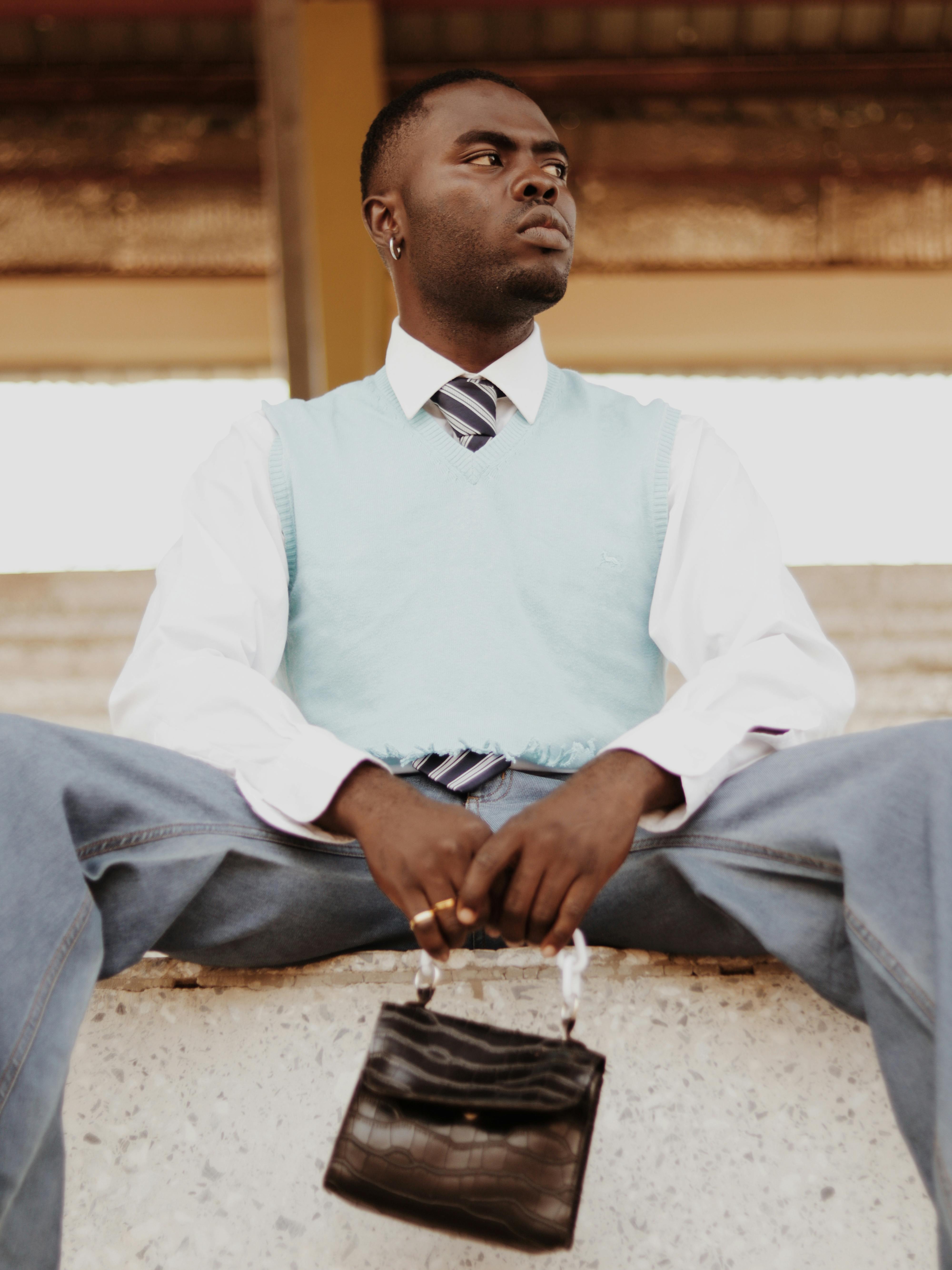 A fashionable man sits confidently with a black bag. Elegant style with a sleeveless sweater.
