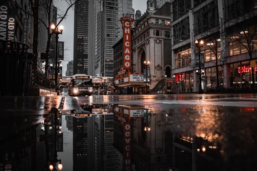 Captivating street view of Chicago Theatre with city lights reflecting in a puddle, epitomizing urban charm.