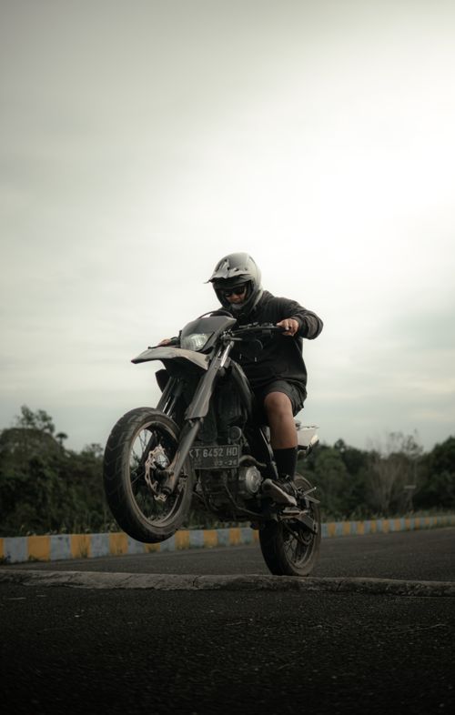 Free A daring motorcyclist performs a wheelie stunt on a motorcycle track, showcasing skill and control outdoors. Stock Photo