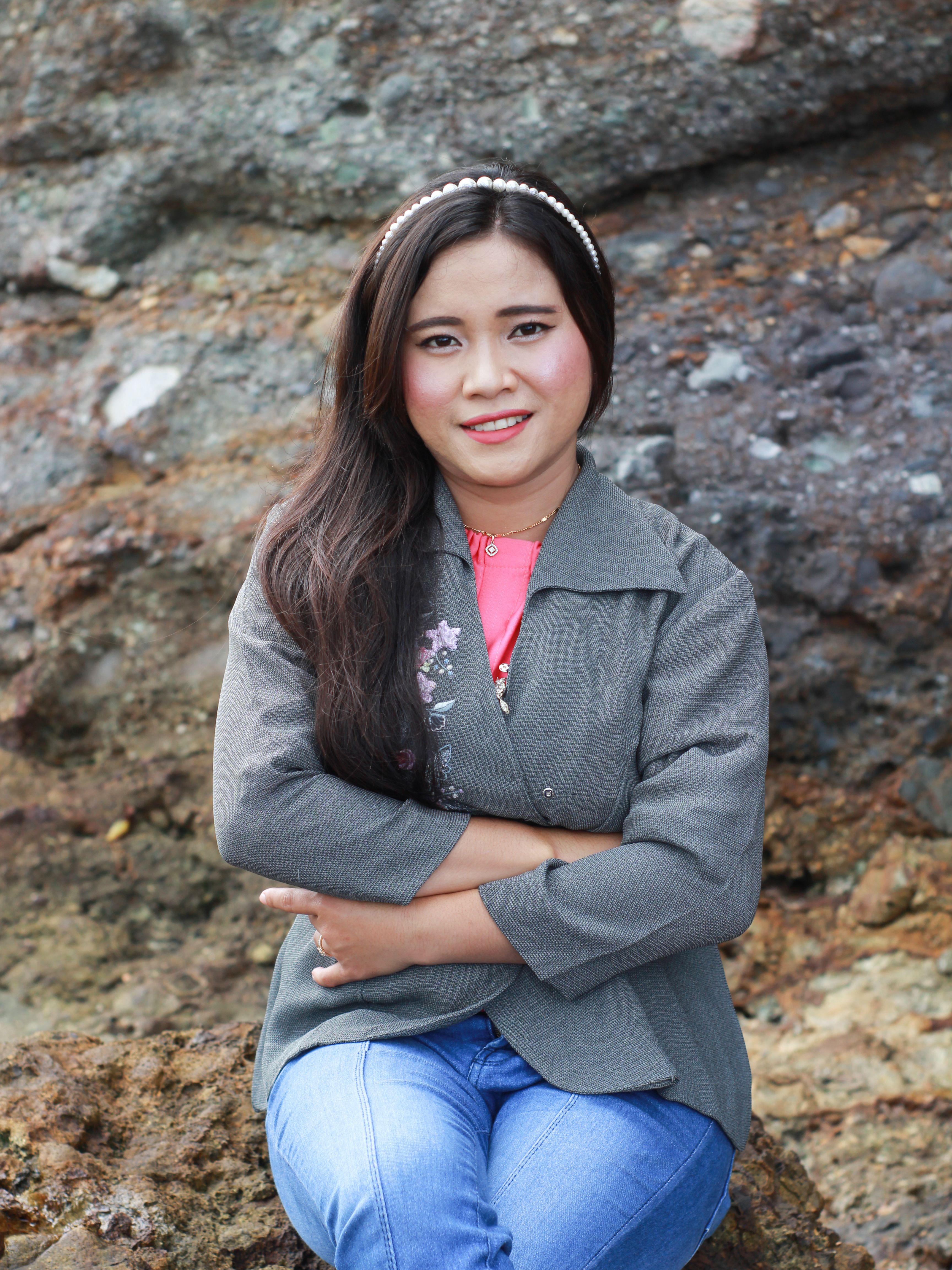 A young woman with long hair and a jacket, sitting on rocks in Badjo, Indonesia.