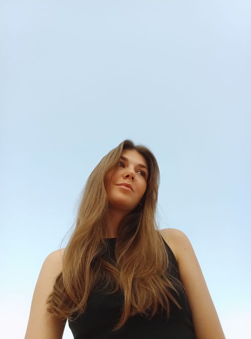 Free Low-angle shot of a woman with long hair and a tank top smiling against a clear blue sky. Stock Photo