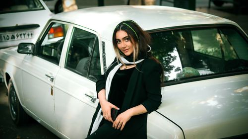 Free Fashionable woman leaning by a vintage car on a Tehran street, exuding urban elegance. Stock Photo