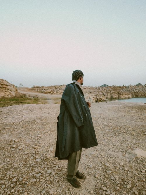 Free Man in a long coat standing on a rocky landscape under a clear sky. Stock Photo