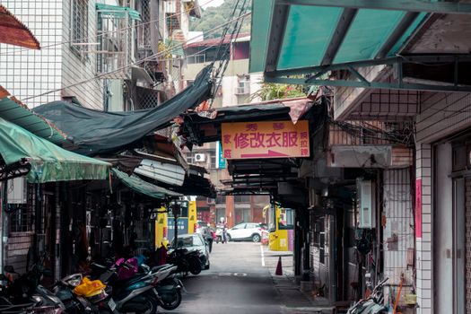 A narrow urban alleyway lined with shops and parked motor scooters, depicting a typical city street scene.