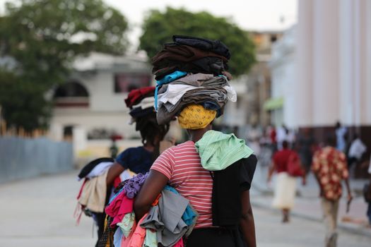 Two women carrying piles of clothes in an urban street, showcasing balance and daily life.