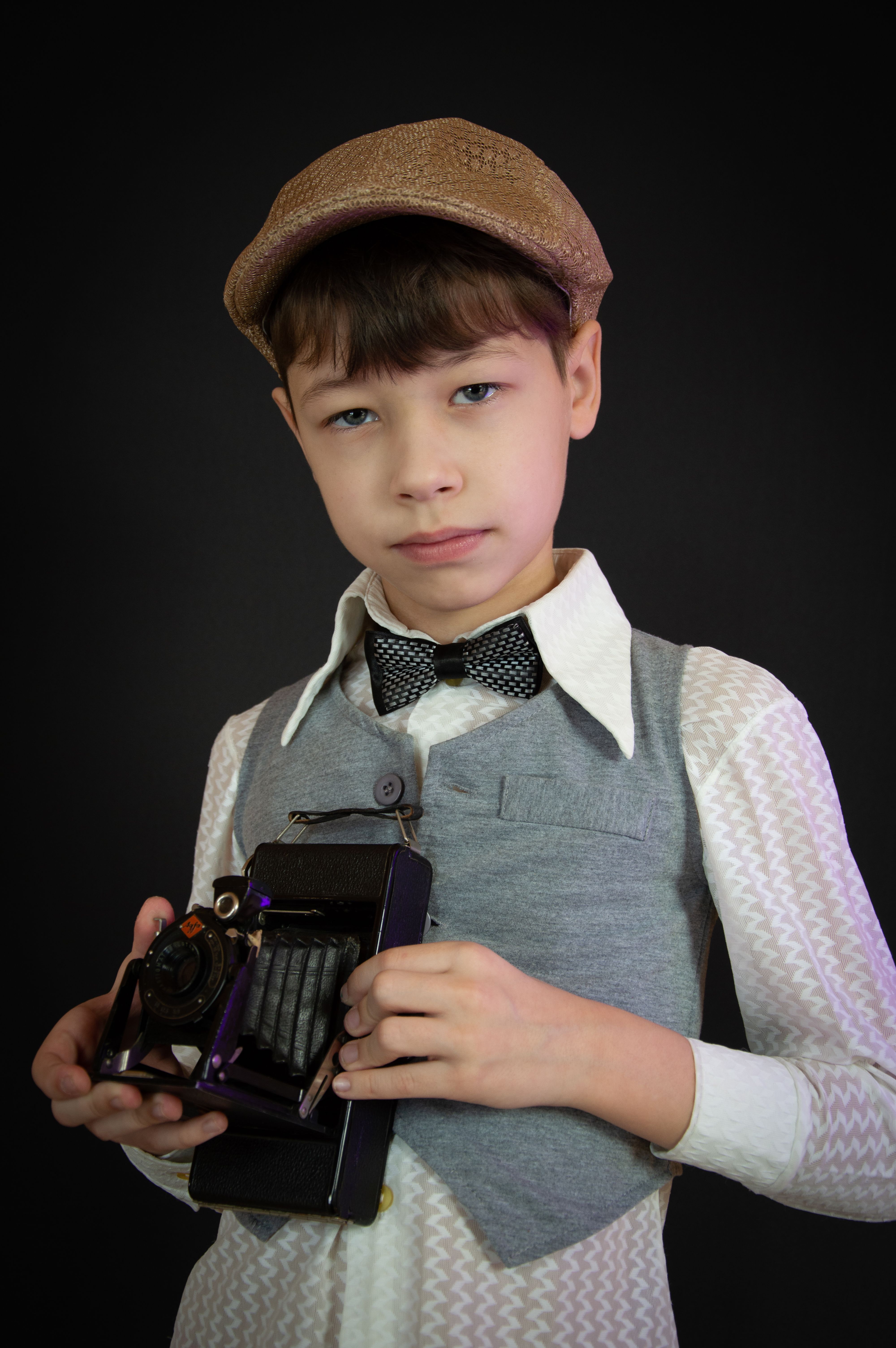 Charming portrait of a young boy in vintage attire holding a classic camera, exuding a nostalgic fashion vibe.