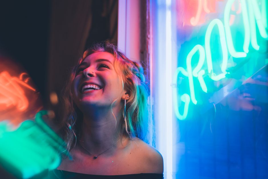 Smiling woman enjoying nightlife with vibrant neon signs, capturing a lively mood.