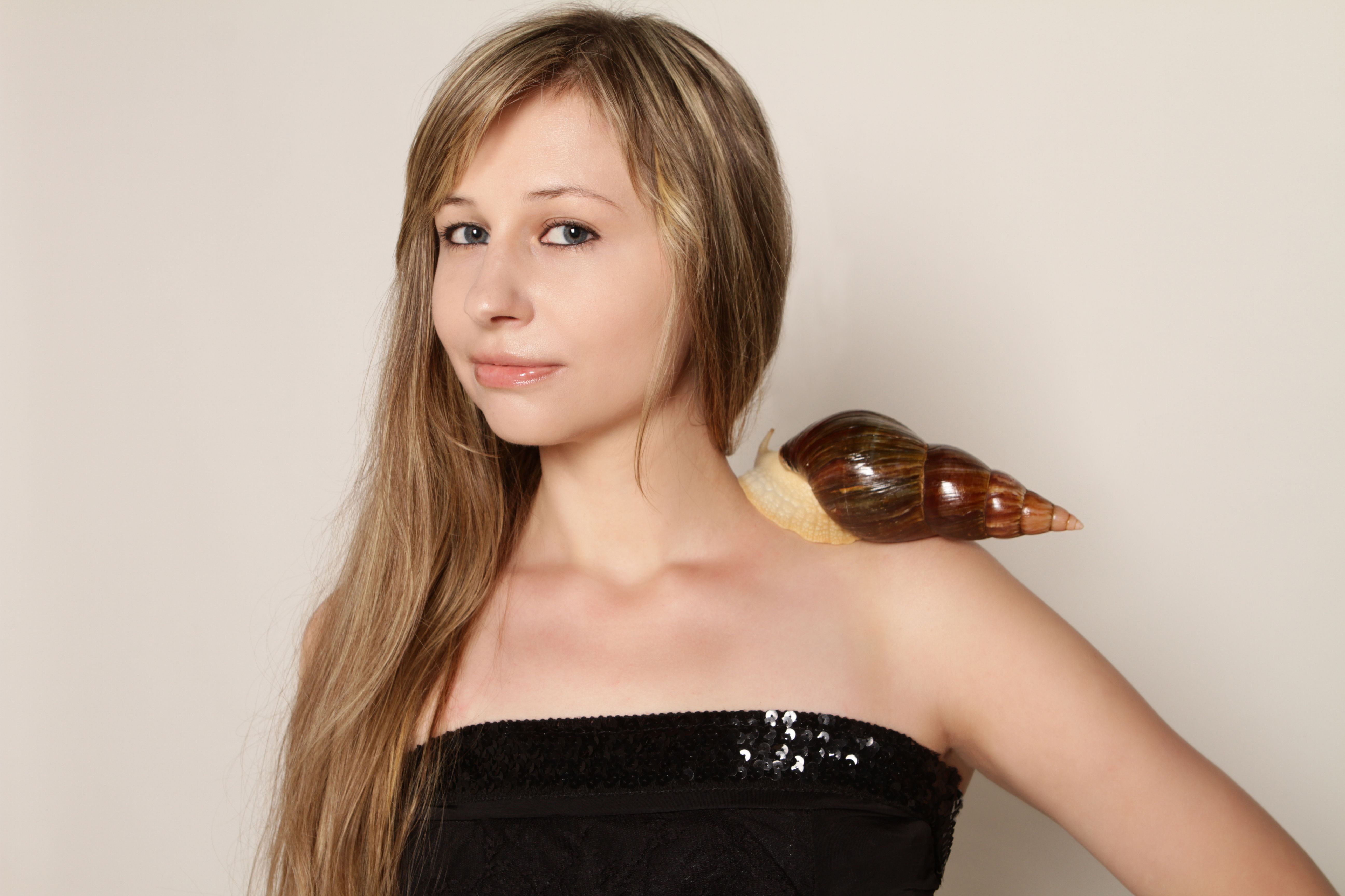 A young woman posing with a giant snail on her shoulder in a studio setting.