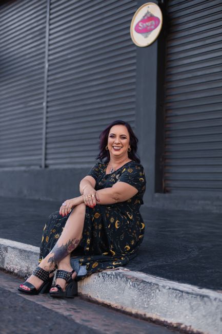 A cheerful woman sitting on curbside in Bauru, SP, Brazil, wearing a stylish floral maxi dress.