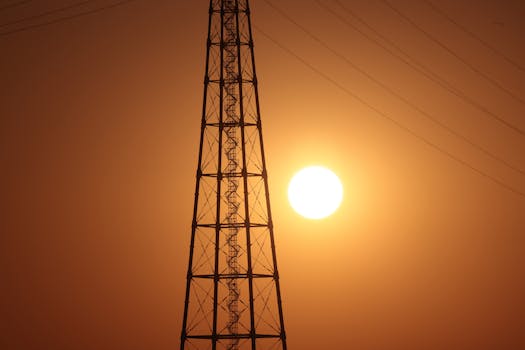 A stunning silhouette of a transmission tower against the vibrant orange sunset sky.