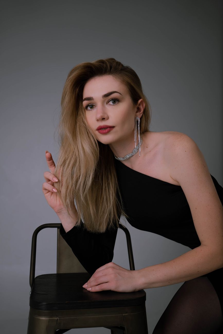 Stylish portrait of a woman in a black dress with elegant jewelry and makeup, posing gracefully indoors.