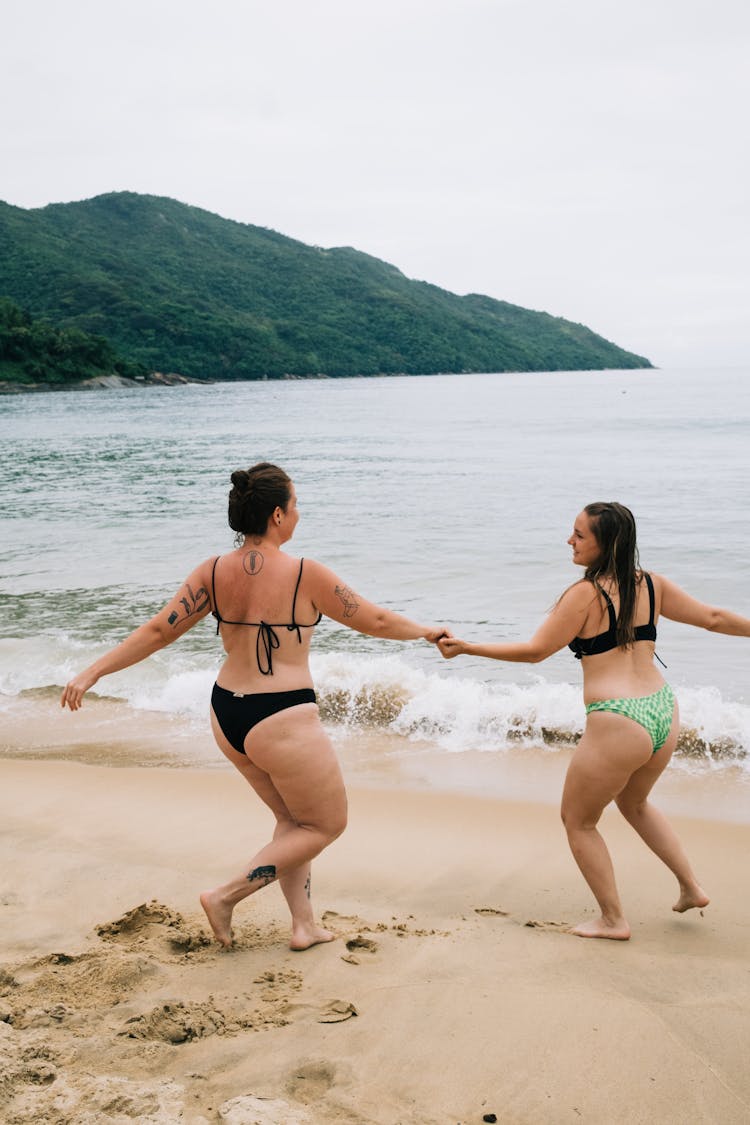 Women Holding Hands And Running On The Beach