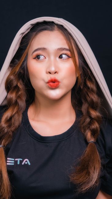 A stylish portrait of a young woman with braided hair and playful expression against a dark background.