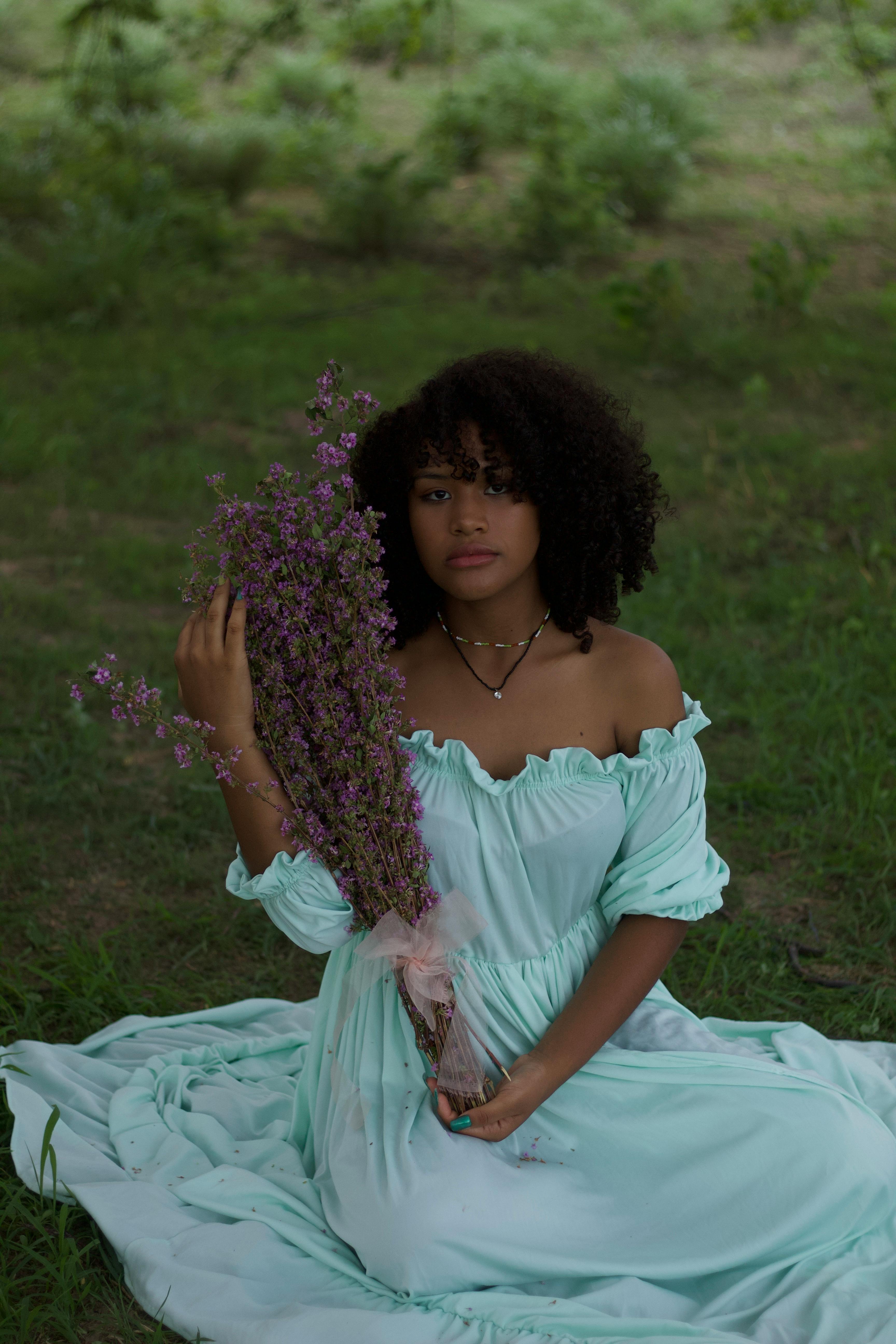 free photo of young woman in a white dress sitting on the ground holding a bunch of flowers