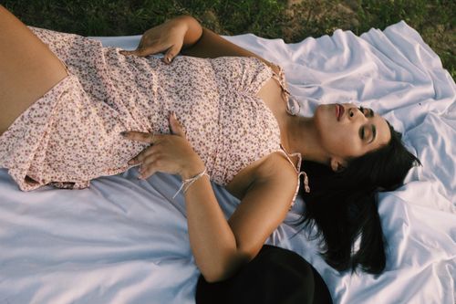 Free Young woman lying on a floral blanket in a sunny park setting, enjoying a peaceful summer day. Stock Photo