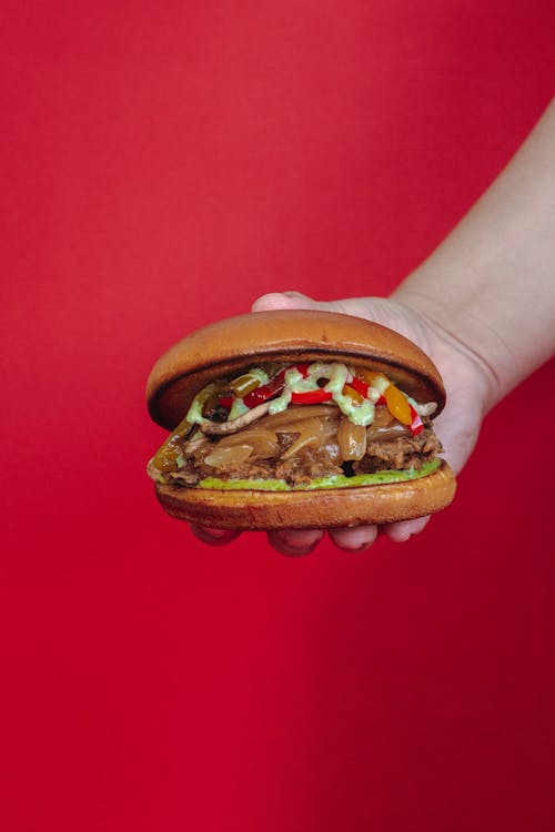 Close-up of a Person Holding a Burger against Red Background 