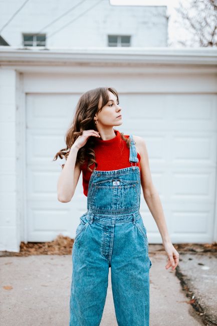 Stylish young woman in denim overalls posing confidently outside a house garage.