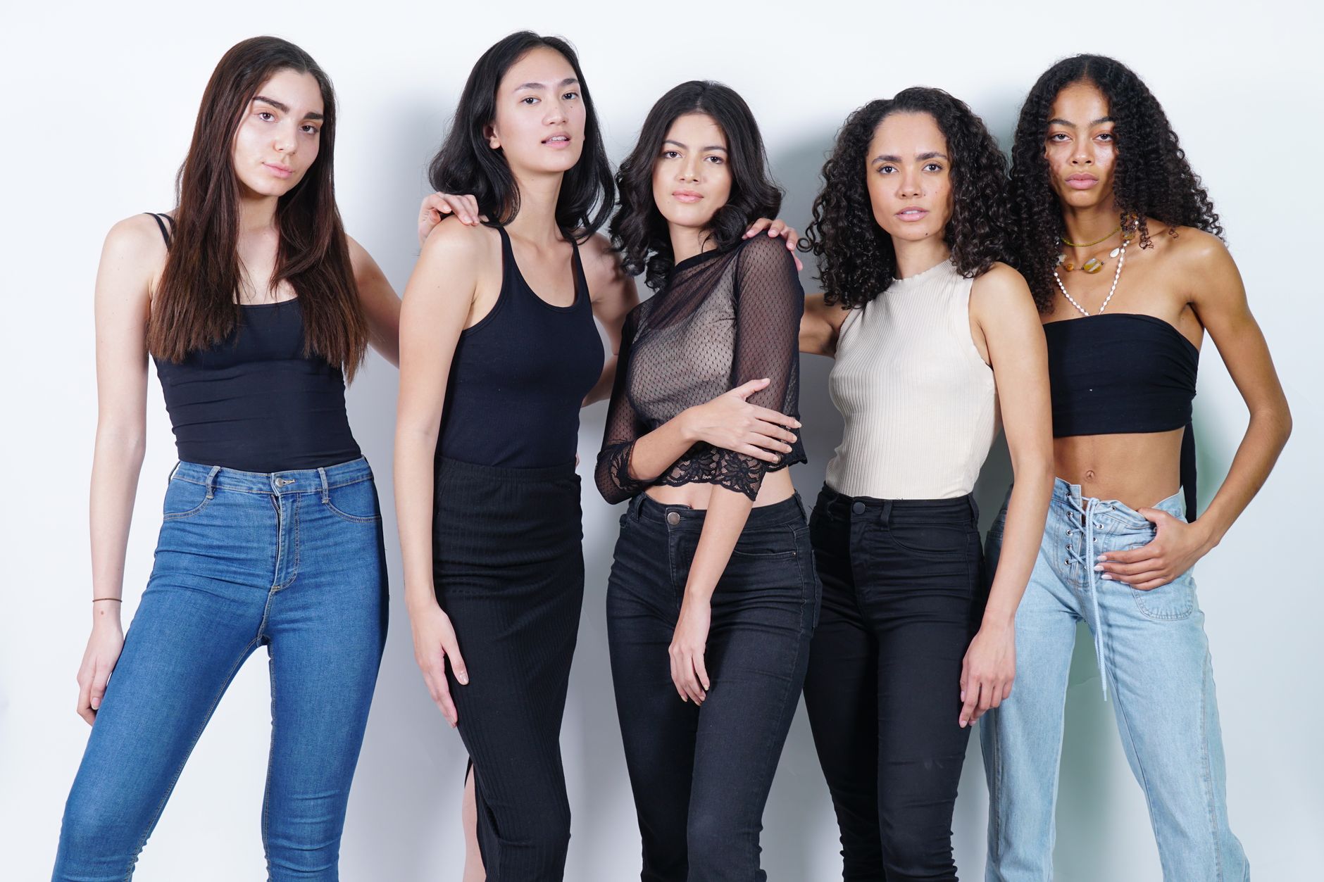 Five young women posing in casual and fashionable outfits in a studio setting.