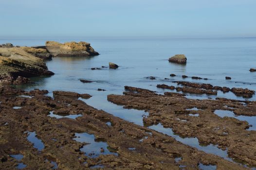 Serene ocean view with rugged rock formations along a tranquil coastline under a clear blue sky.