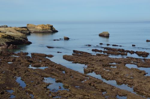 Free Serene ocean view with rugged rock formations along a tranquil coastline under a clear blue sky. Stock Photo