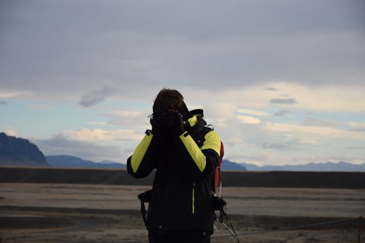 A photographer in warm clothing capturing a dramatic mountain landscape with clouds.