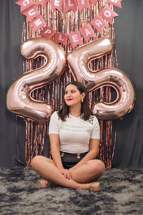 Woman Sitting in front of a Wall with Birthday Decorations and Balloons with Number 25