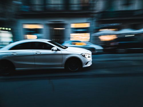Free White car moves swiftly through Barcelona's urban streets, capturing dynamic city life. Stock Photo