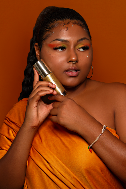 Free Stylish studio portrait of a woman holding a skincare product, showcasing beauty and ethnic jewelry. Stock Photo