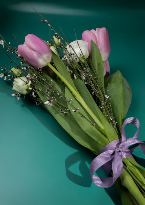 Free A close-up of a vibrant tulip bouquet tied with a pastel purple ribbon on a teal background. Stock Photo
