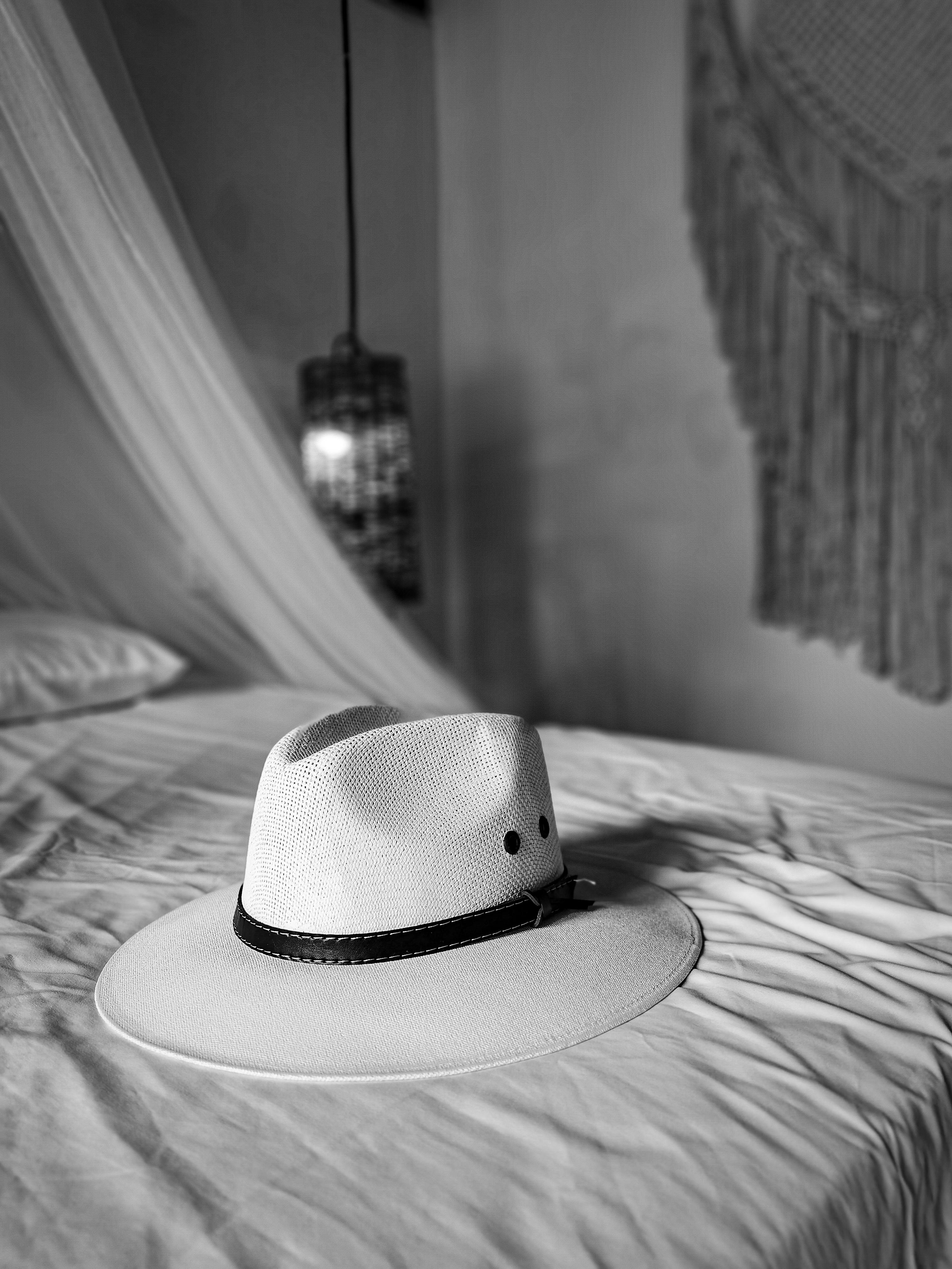 Black and white image of a fedora hat on a bed, capturing elegance and style.