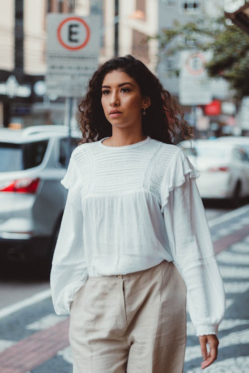 Elegant Woman in a White Shirt Walking on a Sidewalk in City 