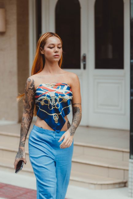 Stylish redhead woman in blue outfit with tattoos walking confidently in Balneário Camboriú.